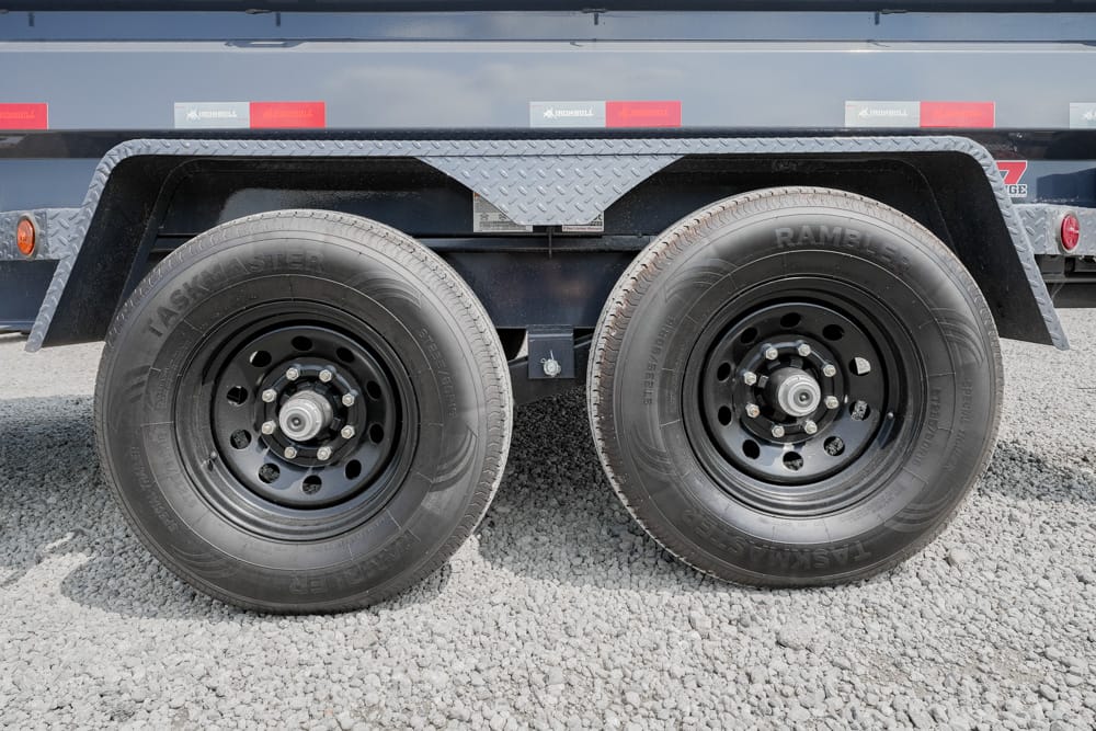 Dual trailer wheels on a heavy-duty flatbed trailer with black rims and exposed lug nuts, parked on gravel (informative image)