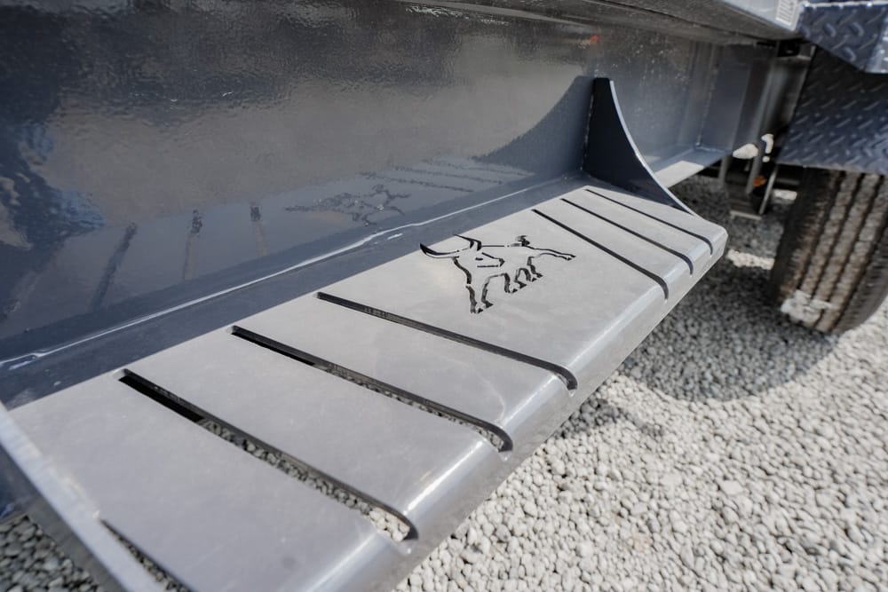 Gray running board on a dark pickup with a Mustang horse logo, laid on gravel.