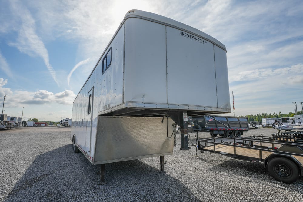 White gooseneck trailer raised on its hitch in a gravel trailer lot, with other trailers and trucks in the background.