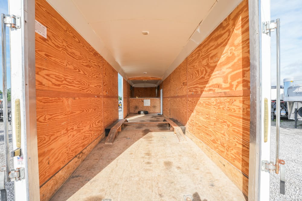Interior of an empty enclosed trailer with wooden walls and floor, two ramps folded down, light from open rear doors