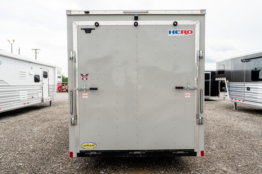 Rear view of a gray enclosed trailer with HERO logo and dual doors on a gravel lot.
