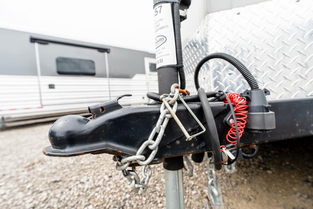 Close-up of a trailer hitch with chains and a red coiled safety cord attached to a black coupler on a diamond-plate trailer.