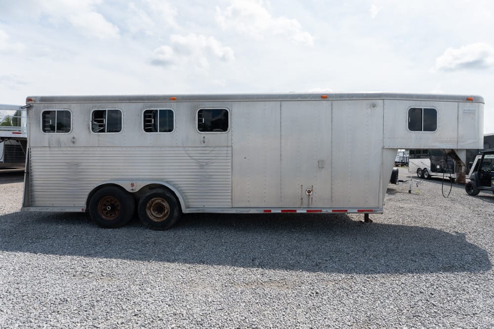 Long silver horse trailer with multiple windows, parked on a gravel lot.