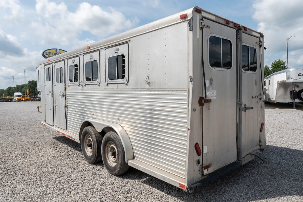 Silver aluminum horse trailer with two side doors and small windows, parked on a gravel lot.