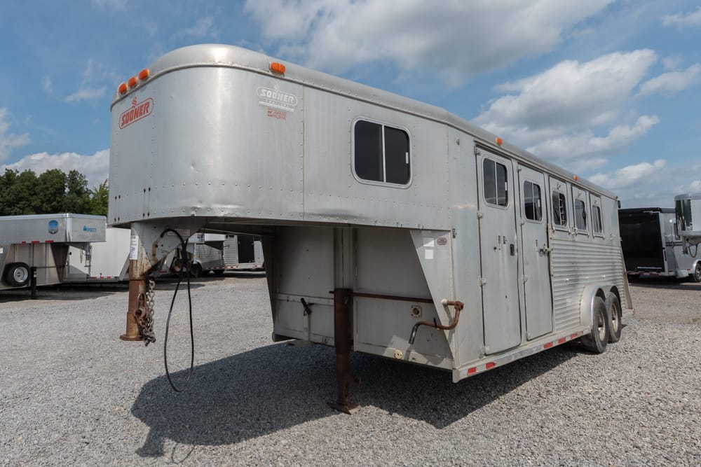 Silver gooseneck horse trailer with rounded front parked on a gravel lot, showing windows and front hitch area