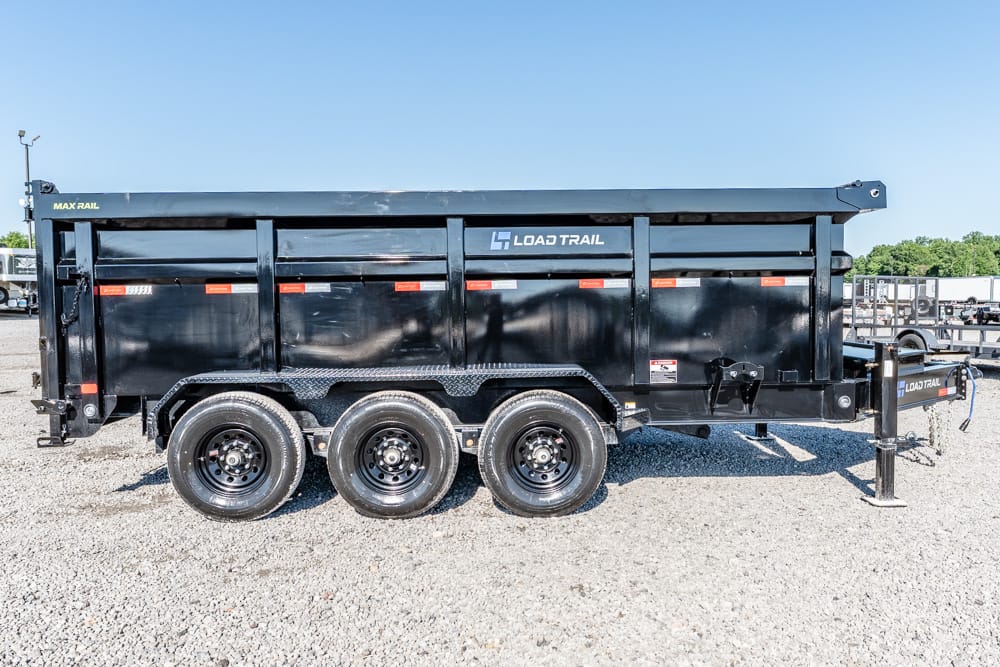 Black Load Trail dump trailer with three axles on gravel, tandem wheels, and a front hitch for towing (Max Rail).