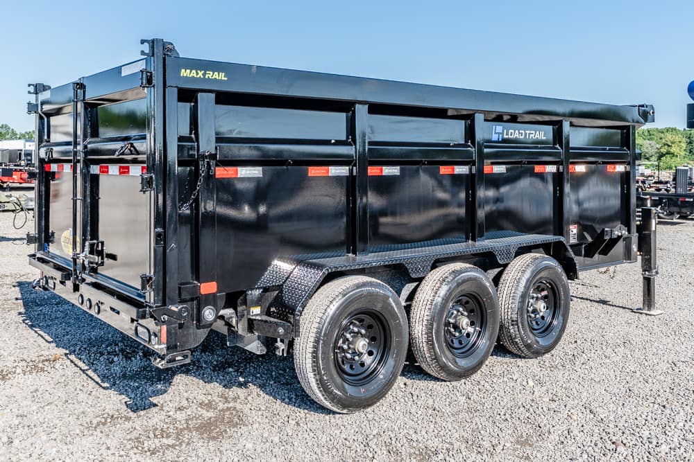 Black three-axle dump trailer on a gravel lot, side view with LOAD TRAIL branding and a yellow MAX RAIL label.