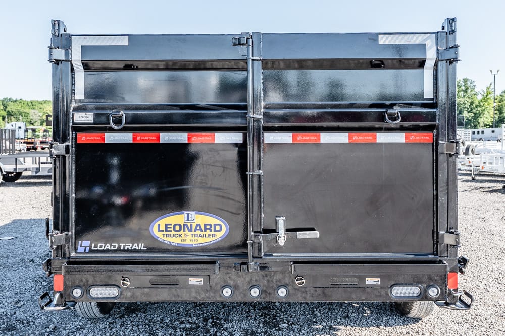 Rear view of a black Leonard dump trailer with Load Trail branding and reflective tape on gravel surface.