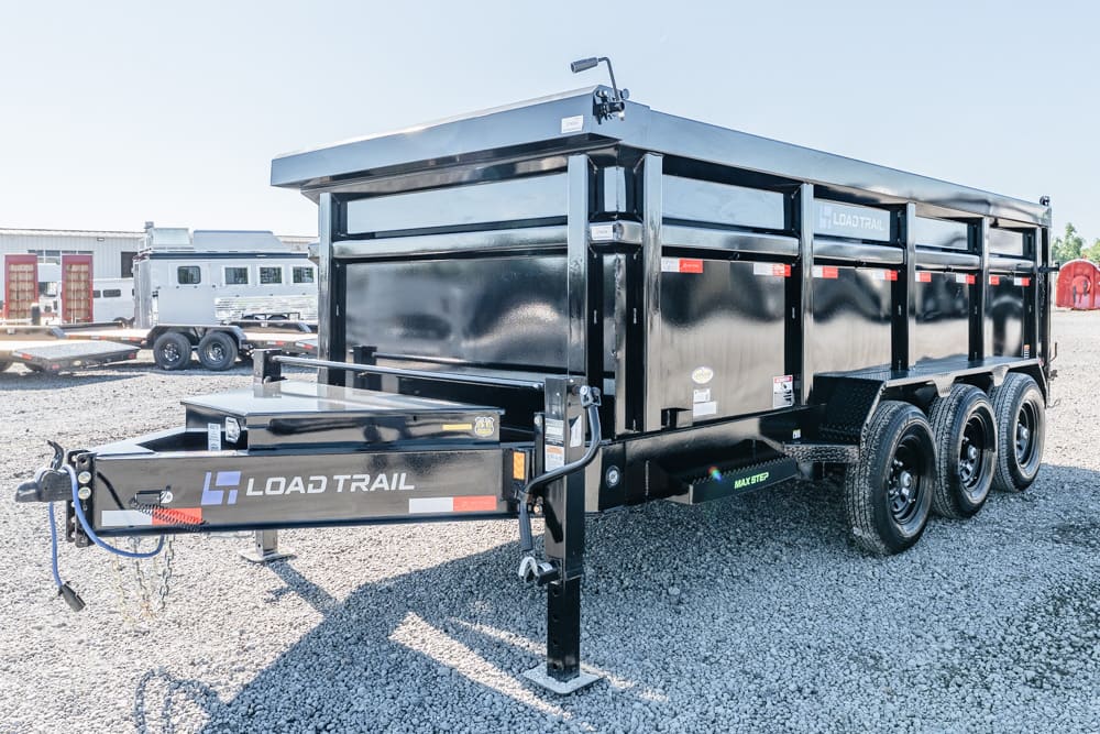 Black Load Trail dump trailer with three axles on a gravel lot, front hitch and safety chains visible.