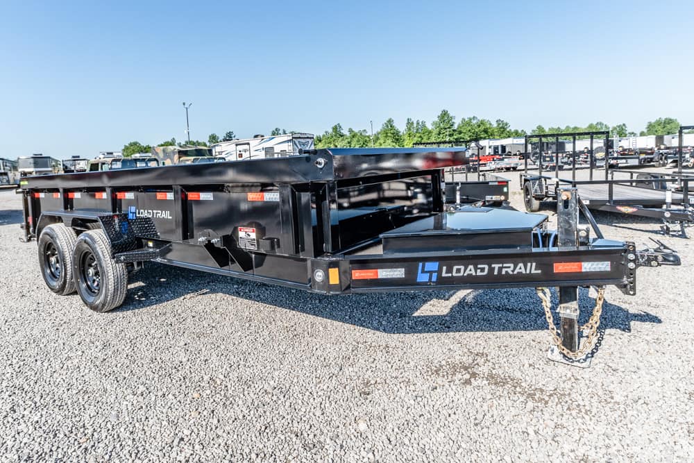 Black Load Trail dump trailer with tandem axles and safety chains in a gravel lot.