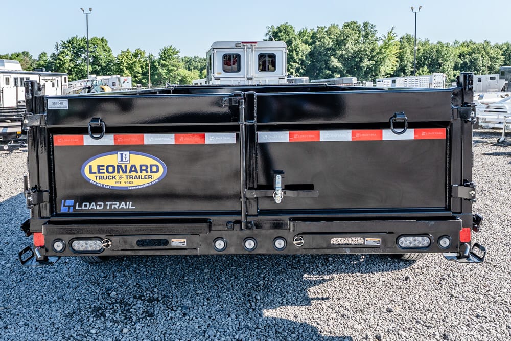 Rear view of a black Leonard Load Trail dump trailer with double doors and reflective red and white stripes in a gravel yard