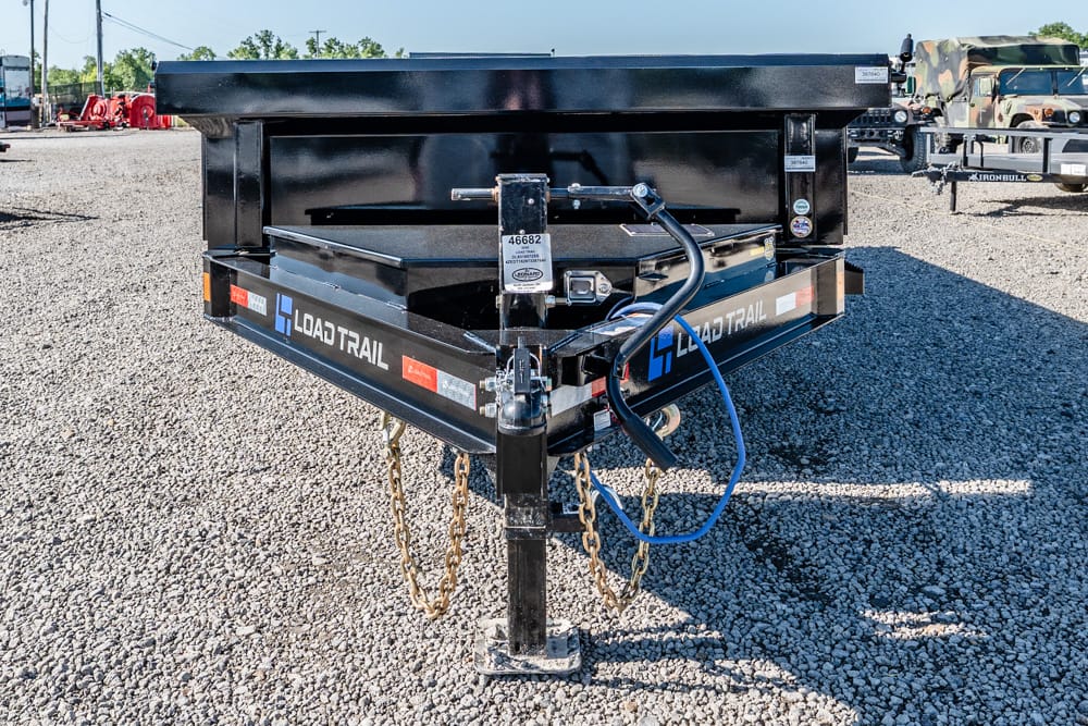 Black Load Trail trailer with front hitch, safety chains, and a blue hose resting on a gravel lot.