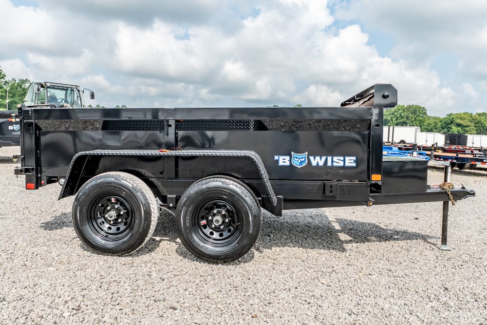 Black dual-axle dump trailer with a Bowise logo parked on a gravel lot, side view