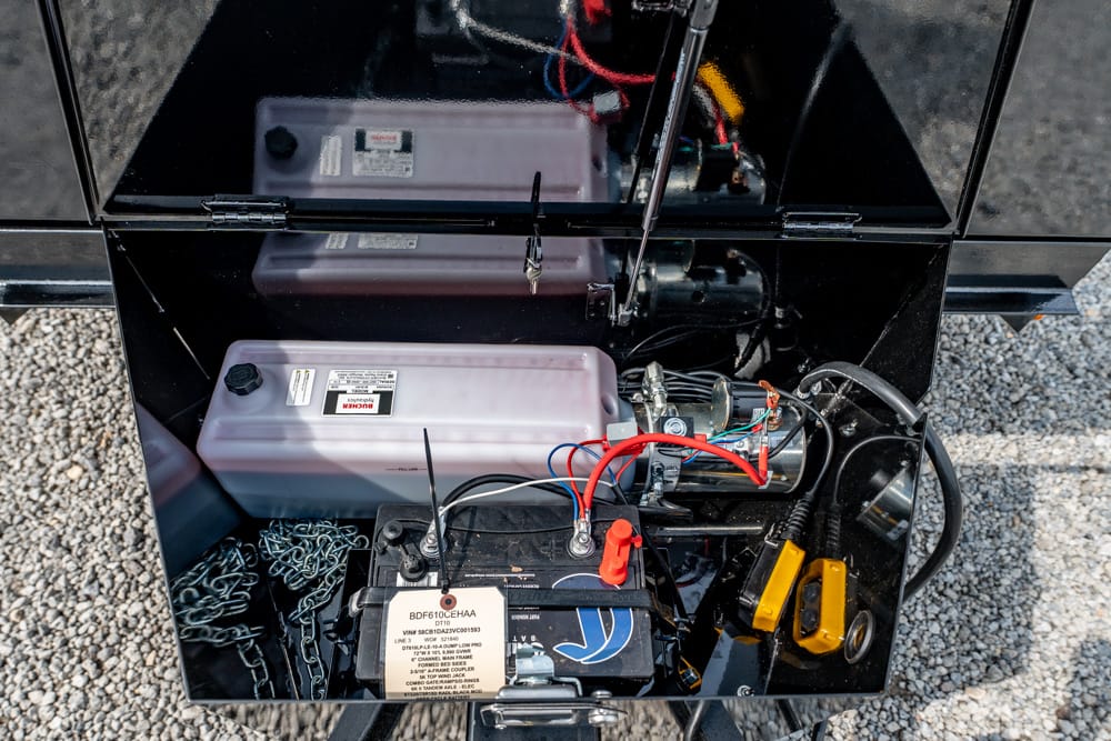 Open compartment of a small generator showing battery, motor, and wiring harness with red/black cables and a protective yellow switch cover inside a metal case.