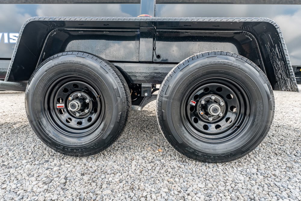 Dual-axle trailer wheels with black steel rims on a gravel surface under a black fender