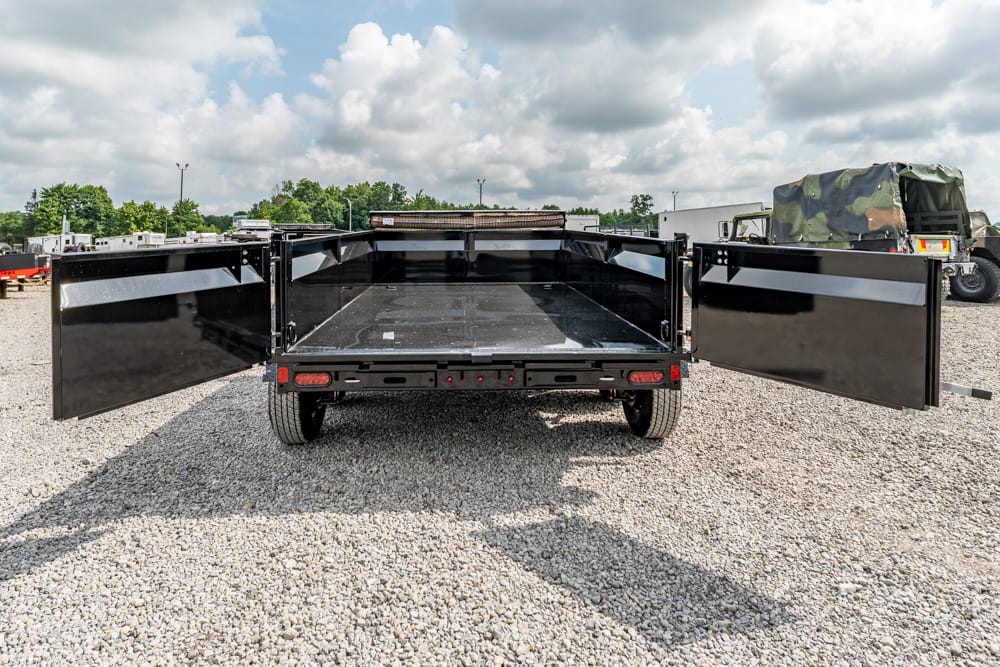 Open-bed dump trailer with wide side doors swung outward, showing a black metal cargo bed in a gravel lot.