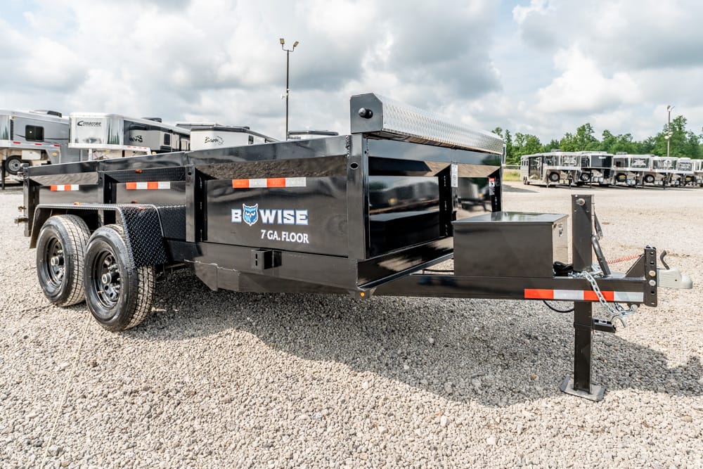 Black BowWise utility trailer with dual axles, diamond-plate toolbox, and front hitch on a gravel lot (hauling equipment).