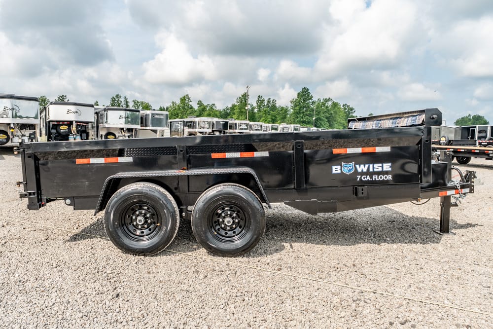 Black dual-axle flatbed trailer on gravel, with orange reflectors and Bow Wise 7 GA Floor branding, ready for hauling.