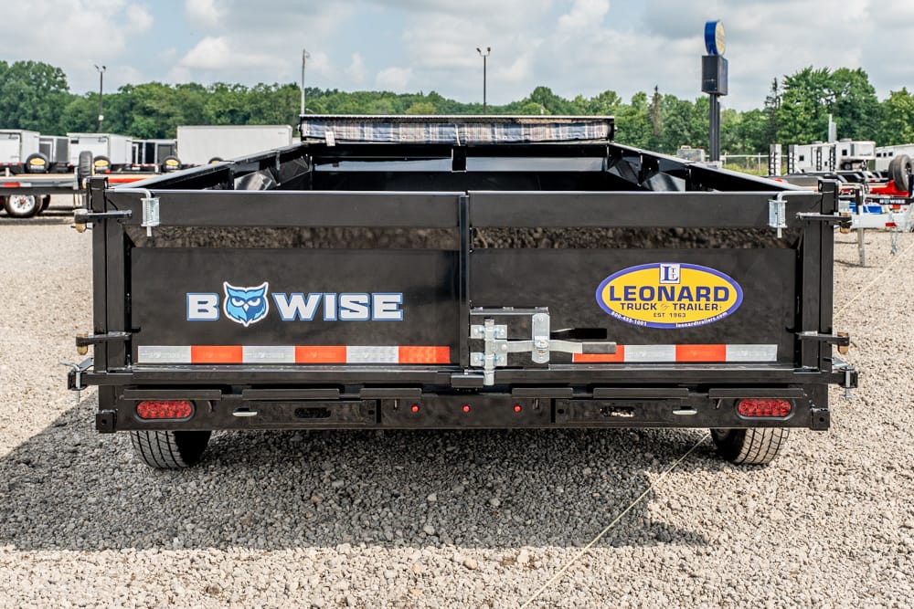 Rear view of a black dump trailer displaying BowWise and Leonard Truck Trailer logos on a gravel lot.