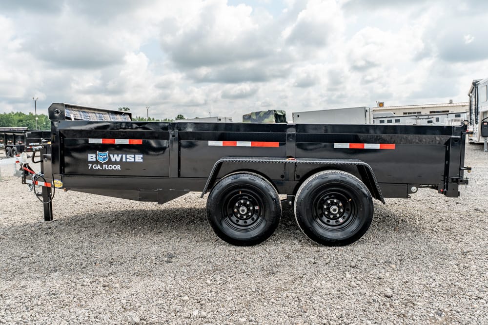 Black dual-axle dump trailer on gravel with reflective red/white stripes and a B-WISE logo on the side surface plate, set in an outdoor lot.