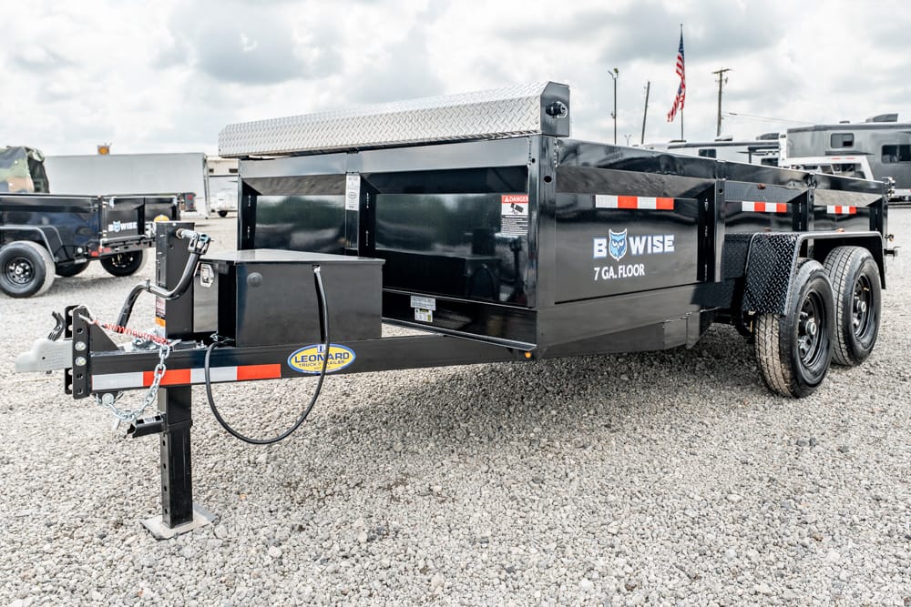 Black dump trailer with dual axles on a gravel lot; front hitch and safety chains visible, logo reads 'BOWISE 7 GA. FLOOR' on the side.