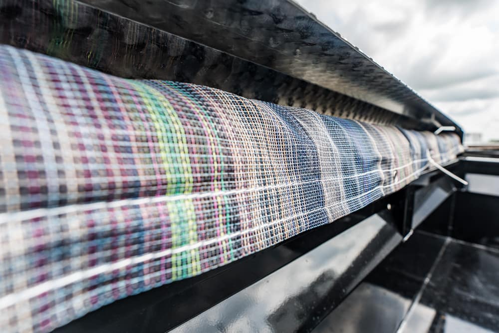 Close-up of a multicolored woven fabric roll on an industrial loom in a factory setting.