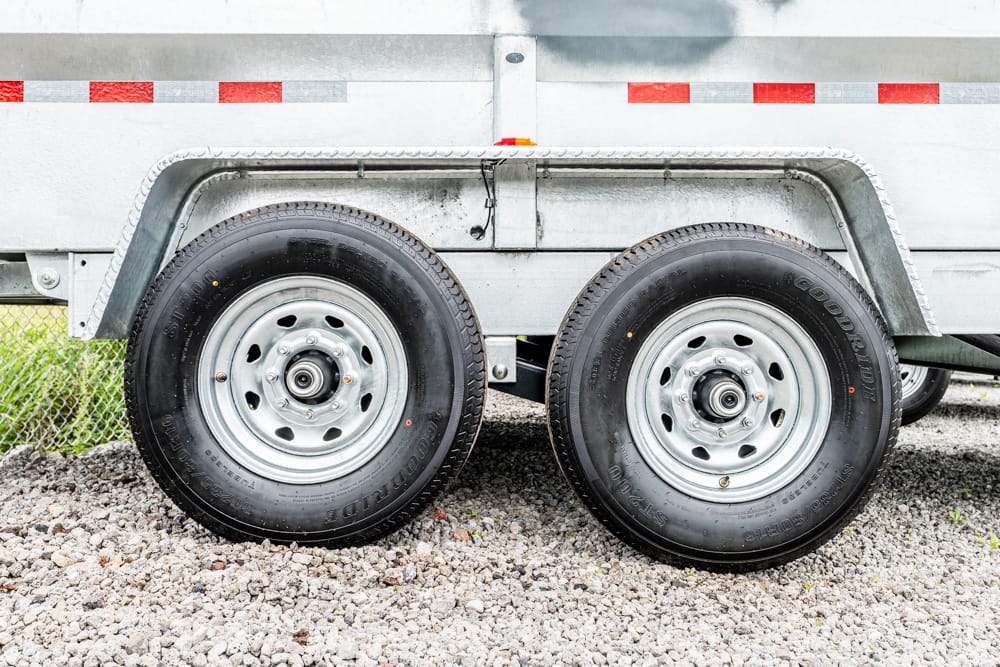 Dual-axle trailer with two wheels, metal fenders, and gravel ground beneath.