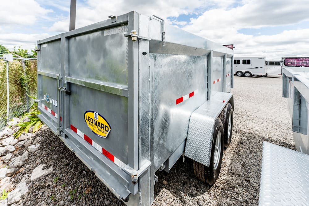 Silver metal utility trailer with dual axles and diamond-plate fenders on a gravel lot, Leonard trailer logo visible on the side.