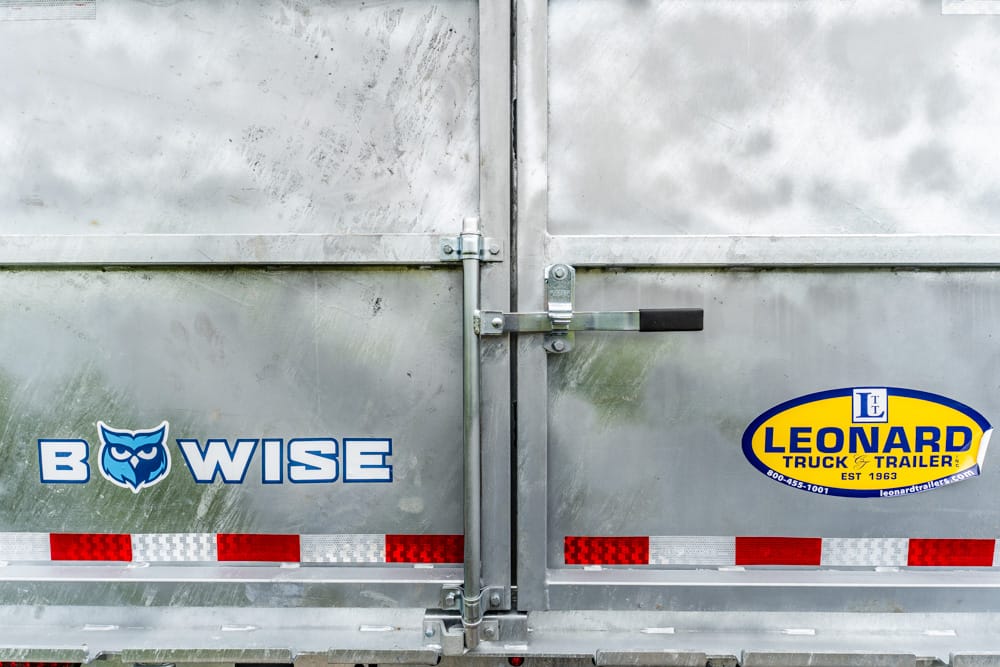 Rear of a silver freight trailer with the blue 'B WISE' logo (owl) and a Leonard Truck Trailer sticker on the door.