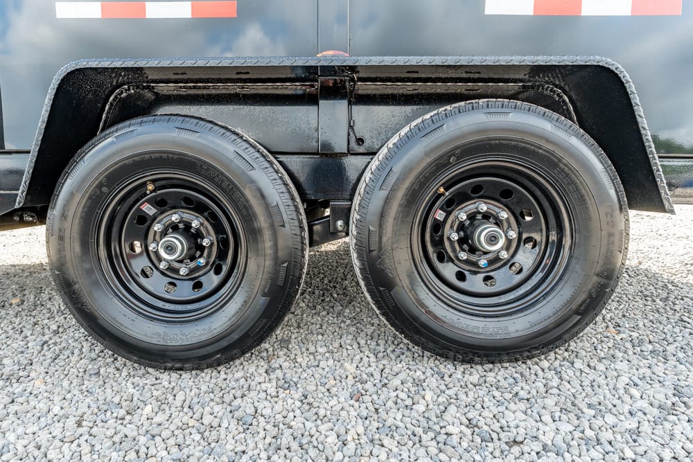 Dual-axle trailer with black steel wheels on a gravel surface, showing a fender and red/white reflective tape strip above the wheels.