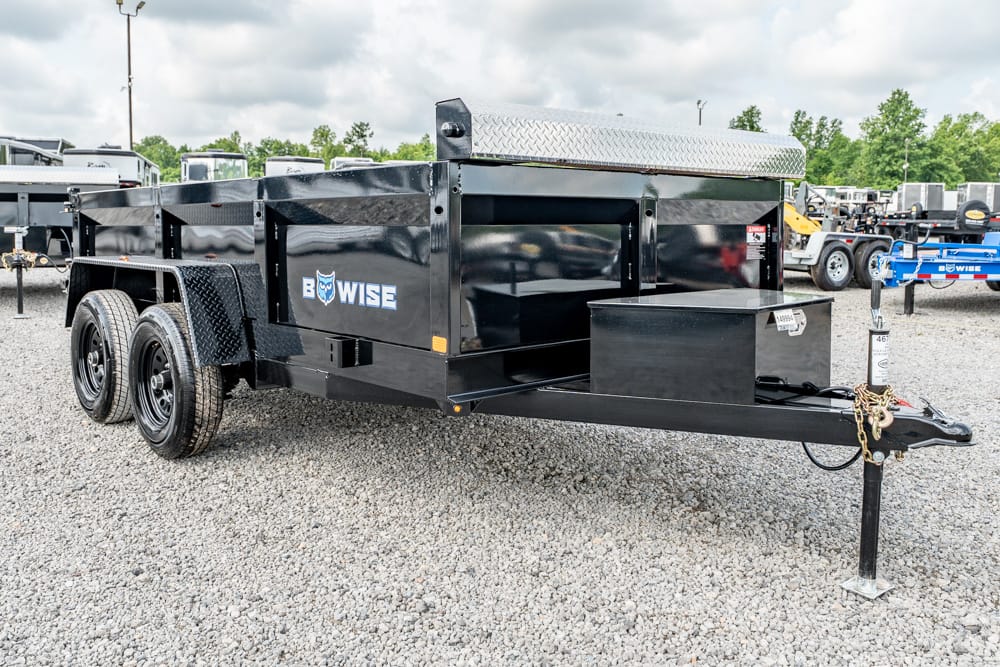 Black dual-axle utility trailer with storage box and diamond-plate toolbox, on a gravel lot (BowWise branding)