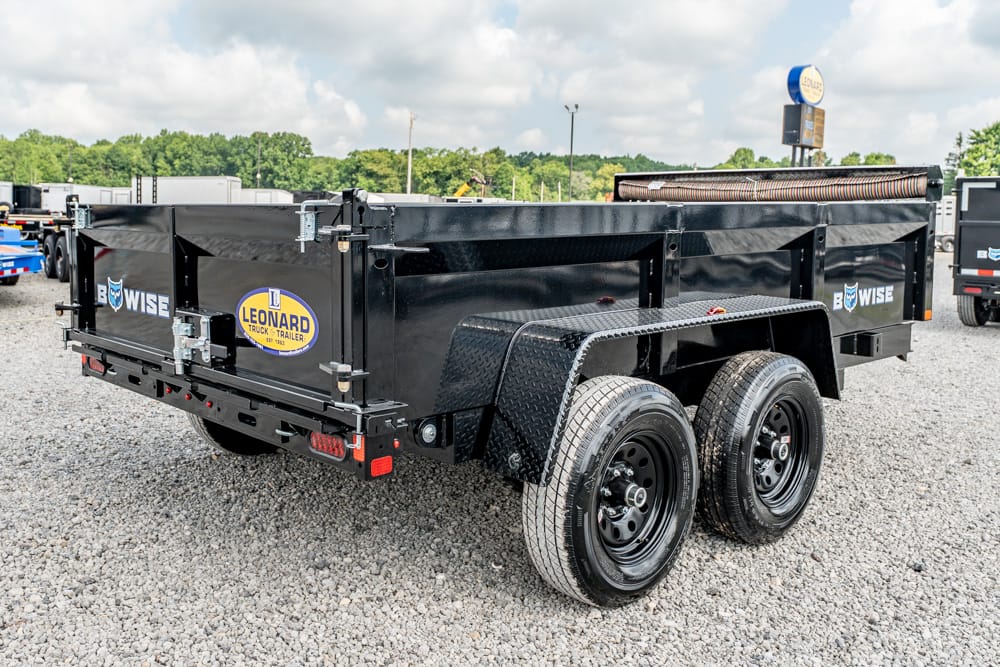 Black dual-axle dump trailer with metal fenders and Leonard logo parked on gravel.