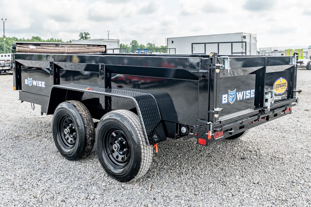 Black Bowise tandem-axle utility dump trailer on a gravel lot, with a side ladder and spare roller on top.