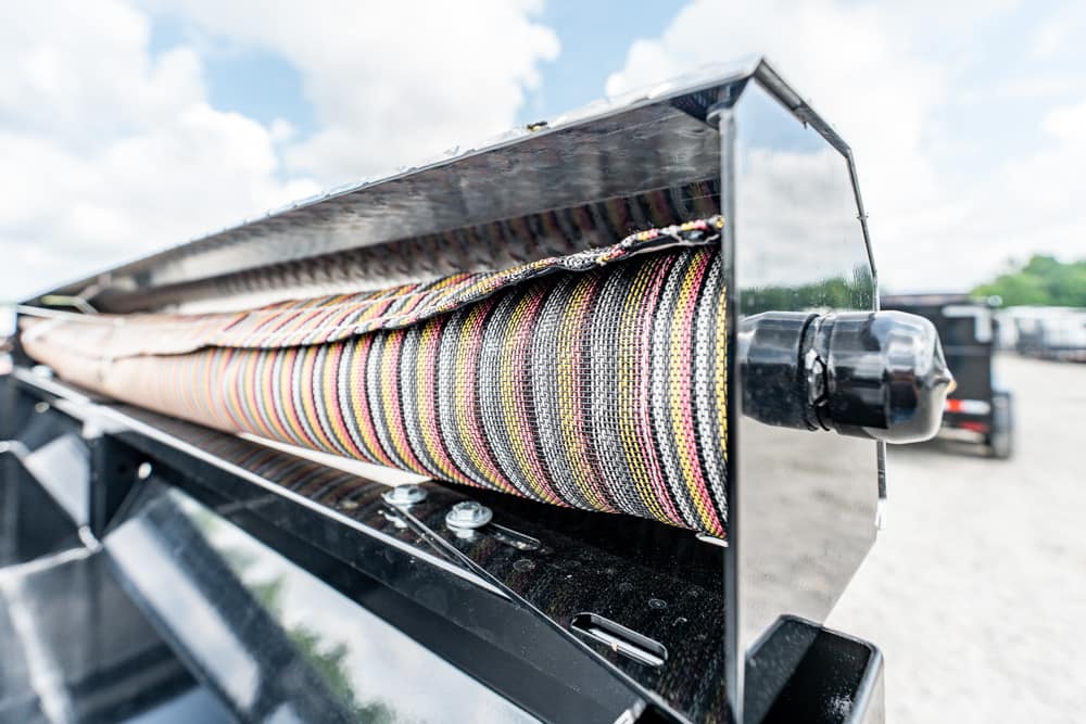 Close-up of a multi-colored braided cable reel inside a metallic housing on a trailer or truck, highlighting the organized wiring bundle and chrome finish, outdoors under a cloudy sky