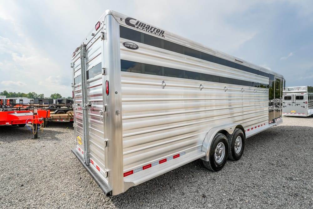 Two-axle aluminum horse trailer parked on a gravel lot, viewed from the rear-left side.