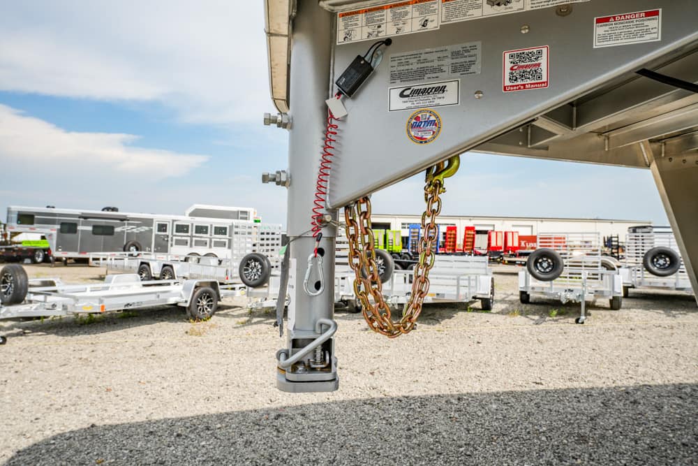 Close-up of a trailer hitch with safety chains and wiring attached to a metal frame in a trailer yard