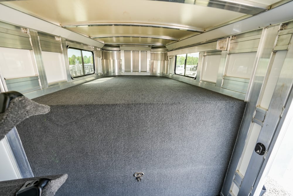 Empty aluminum trailer interior with a grey carpeted floor, side windows, and open rear door seen from the doorway entrance.
