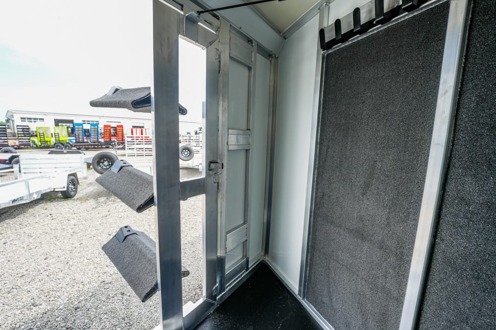 Interior of a metal trailer with foam-lined wall panels and a doorway, view of a gravel lot with parked trailers outside.