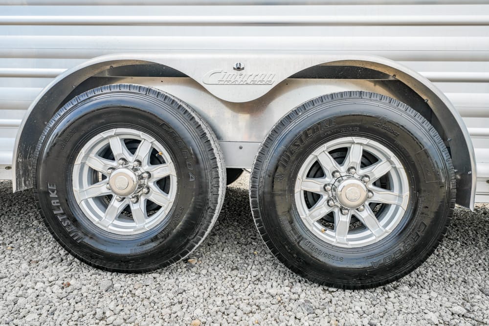Dual trailer wheels on a gravel surface with a curved metal fender above the tires.
