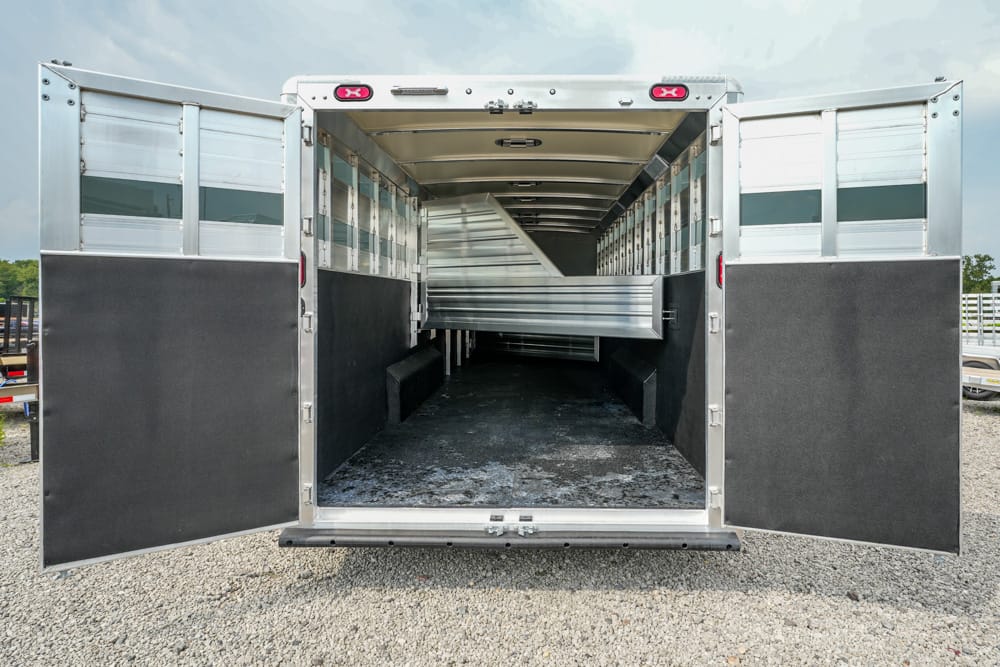 Open horse trailer with interior ramp and divider, ready for loading on a gravel lot