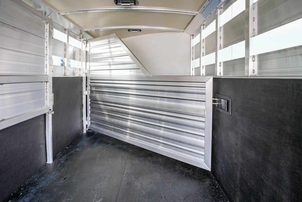 Interior of aluminum horse trailer with a metal divider and black rubber floor mats.