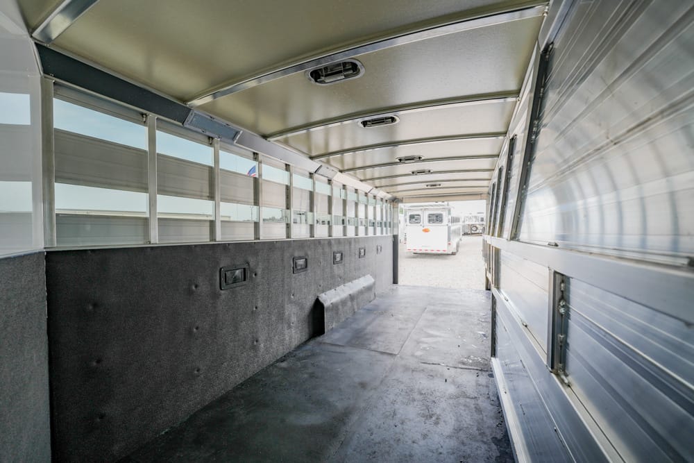 Interior of an empty metal transport trailer with side windows and a rear ramp visible at the far end.