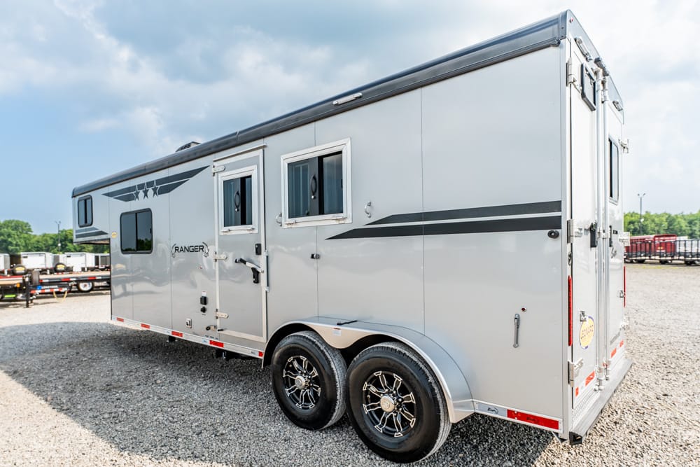 Silver travel trailer with two black-wheeled axles parked on gravel, side door and windows visible (Ranger branding)
