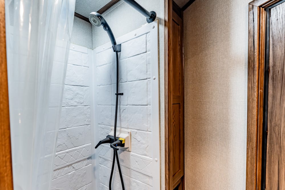 Shower stall with a handheld shower head mounted on a white wall panel, next to a partially drawn curtain in a small bathroom.