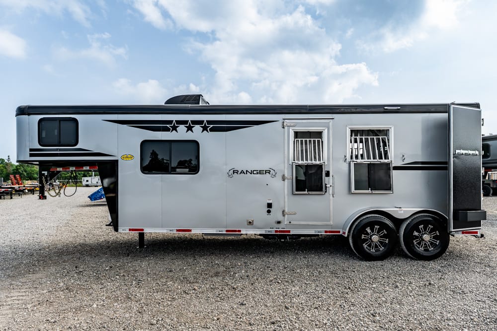 A silver Ranger travel trailer with two axles parked on gravel, side door and barred windows visible.