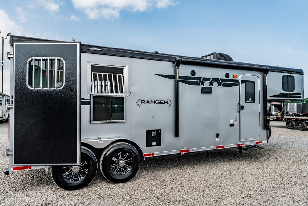 Grey Ranger travel trailer with black trim and star decals, parked on gravel with two axles and a large back door open or extended ramp at the rear park area.