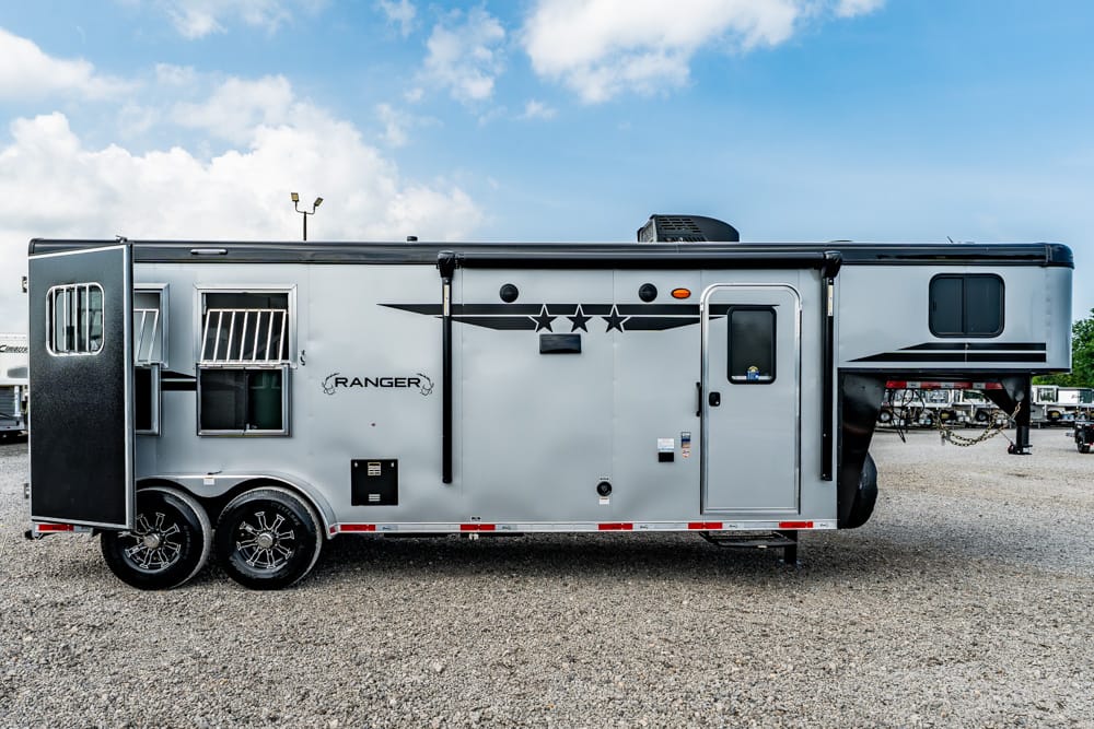 Silver Ranger horse trailer with living quarters parked on gravel; side door closed and windows visible on a bright day.