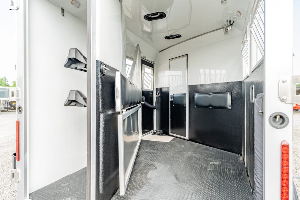 Interior of a two-stall horse trailer with padded partitions, rubber mat floor, and a doorway at the back.