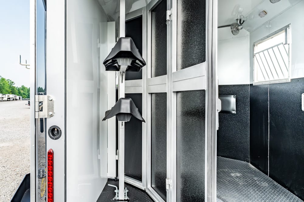 Interior of a horse trailer with metal divider walls, padded stalls, and a diamond-plate floor visible near the entry.