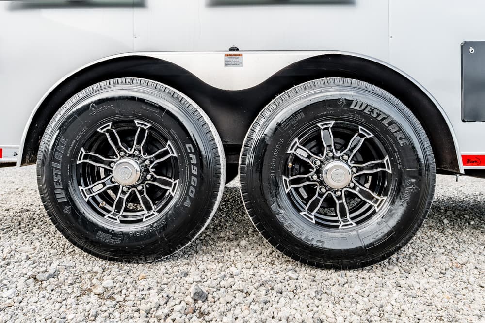 Dual trailer wheels with black rims on a gravel surface beside a silver trailer weight-bearing tires detail